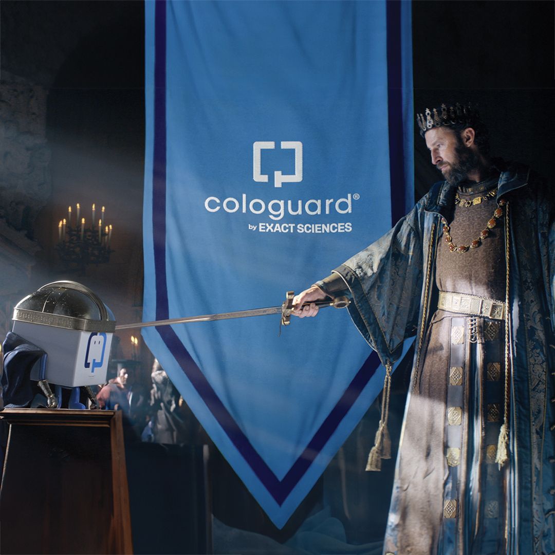 A king knighting a Colorguard test on a pedestal with a sword, with a Colorguard banner in the background.
